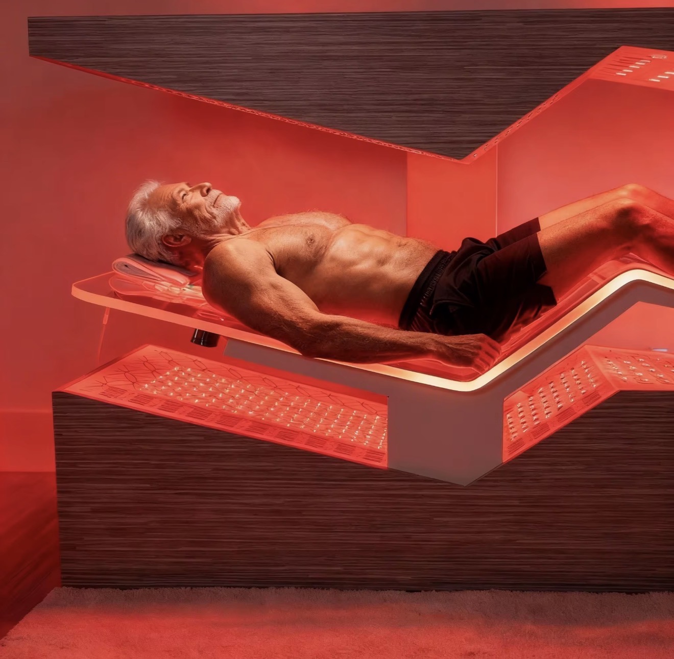 A person lying on The Immortal zero-gravity bed under full red light therapy panels